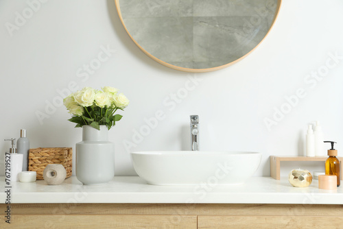 Vase with beautiful white roses and toiletries near sink in bathroom