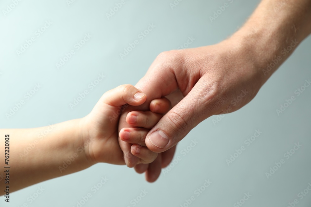 Father and child holding hands on light blue background, closeup