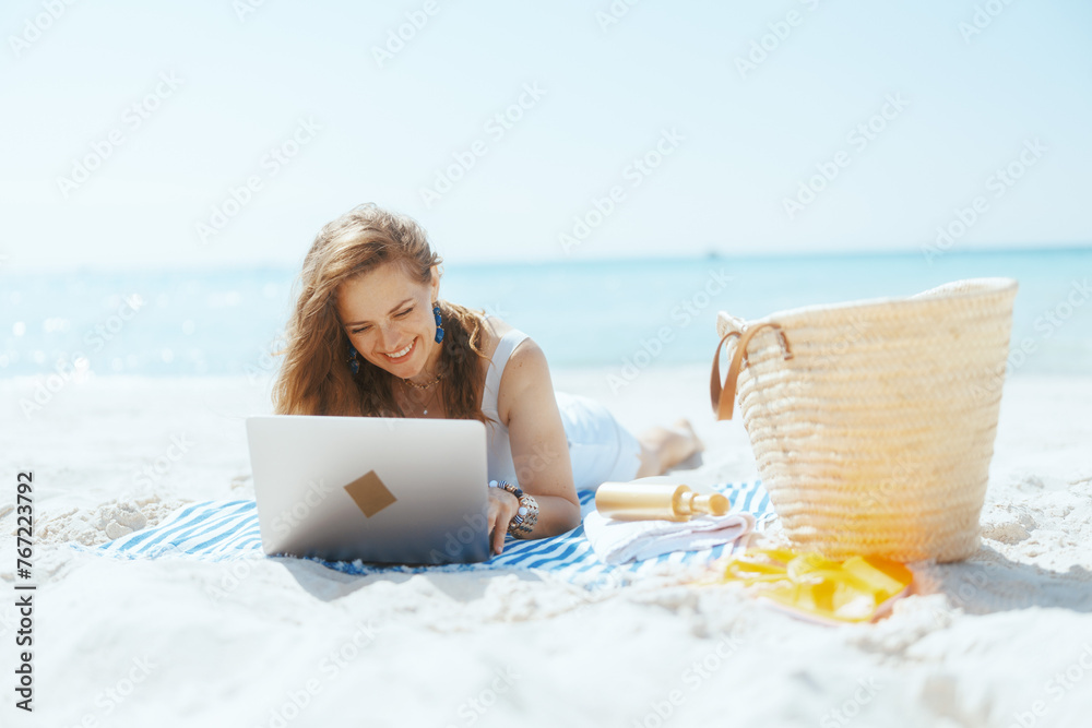 smiling modern woman on ocean coast using laptop