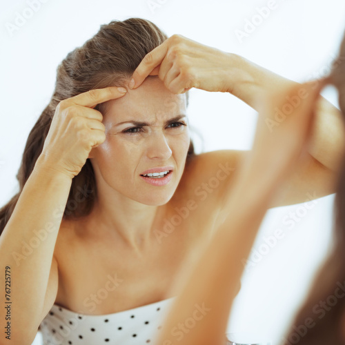Concerned young woman squeezing acne in bathroom