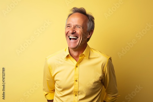 Portrait of happy senior man laughing and looking at camera on yellow background