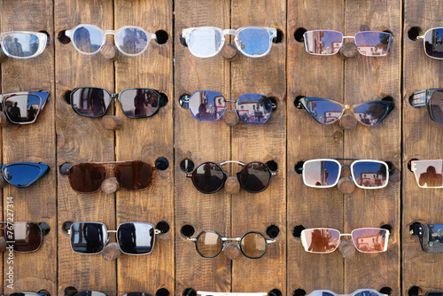 Assortment of Sunglasses on a Wooden Display. Various styles of sunglasses neatly arranged on a rustic wooden stand at a street market.