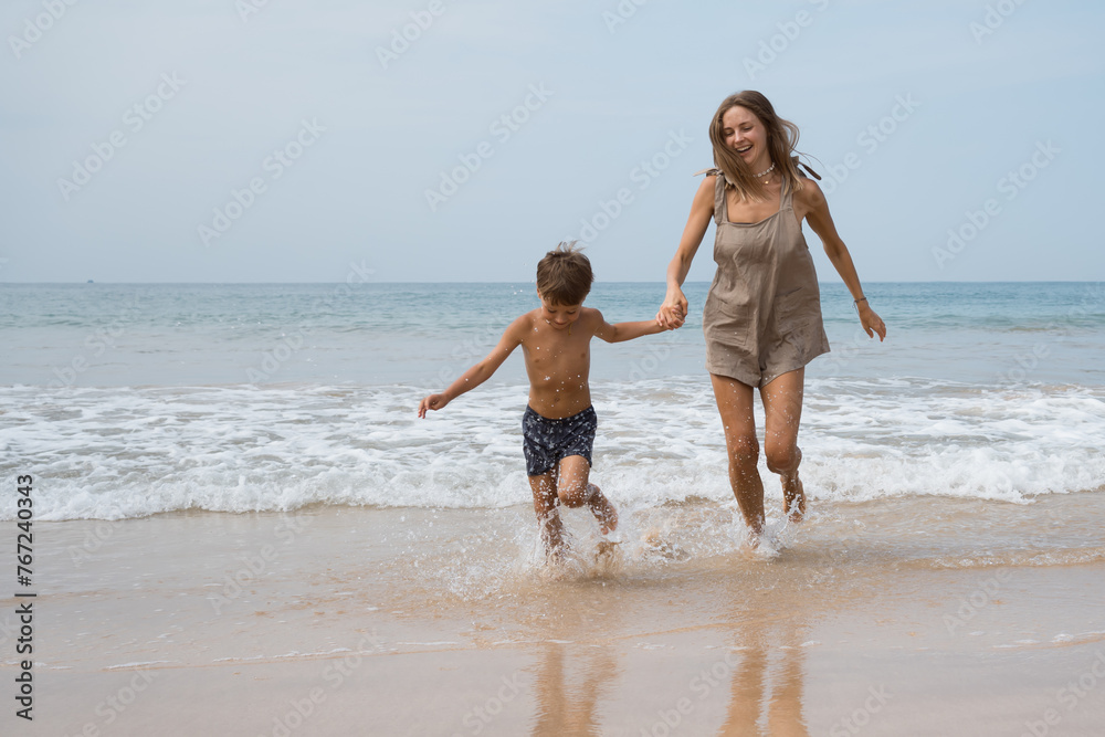 Happy beautiful young mother plays with her son in sea waves Happy beautiful young mother plays with her son in sea waves