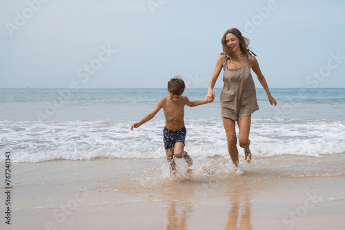 Happy beautiful young mother plays with her son in sea waves
