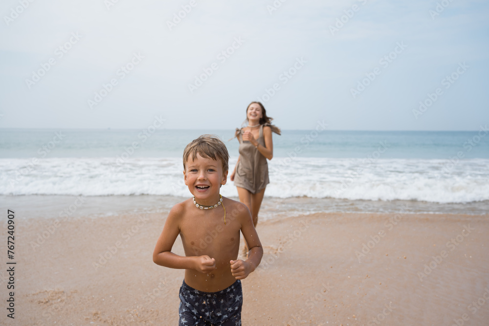 Happy boy and mother running and playing on sea beach at summer