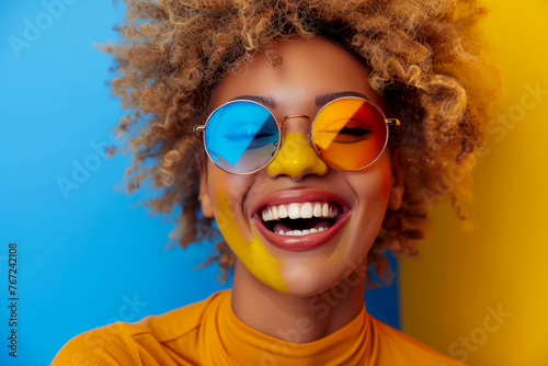 Joyful African American woman with blonde afro hair and funky glasses, laughing and radiating happiness in colorful fashion