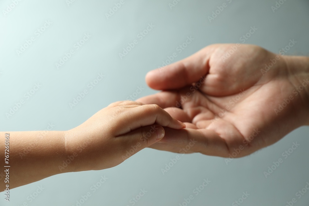 Father and child holding hands on light blue background, closeup Father and child holding hands on light blue background, closeup