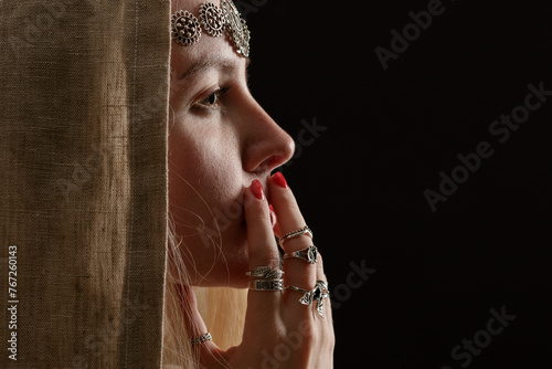 Colored mystical portrait in profile of a young woman wearing a hood and occult jewelry.