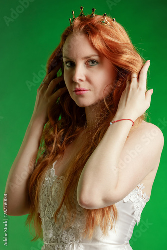 Portrait of a red-haired young woman with a crown on her head on a emerald background