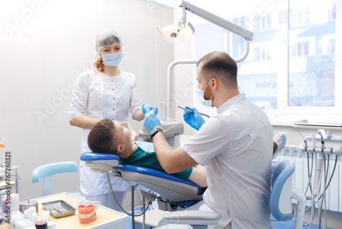 Dentist with assistant using equipment for examination of teeth of man patient. Young men getting dental checkup in dentistry clinic