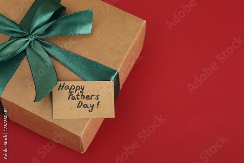 Happy Father's Day. Gift box and card with greetings on red background, closeup. Space for text photo