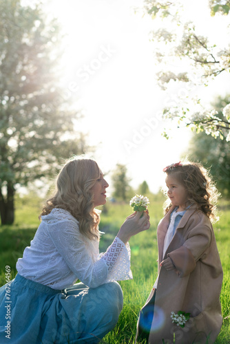 A young beautiful mother and her little daughter are picking flowers in the meadow