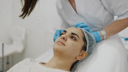 The hands of a cosmetologist wipe a woman's face before a cosmetic procedure