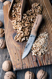 Crushed walnut nuts kernels and knife on wooden plate close up. Food photography