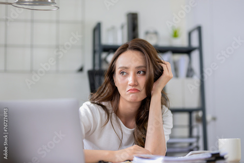 Businesswoman looks stressed, bored and holding her head. Indicates a headache while working at a desk in home office.