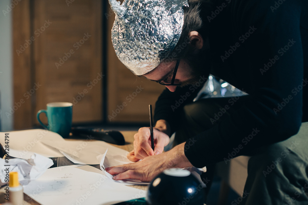 Symbolic Secrets: Man in Tin Foil Headgear Sketching Esoteric Signs - obrazy, fototapety, plakaty 