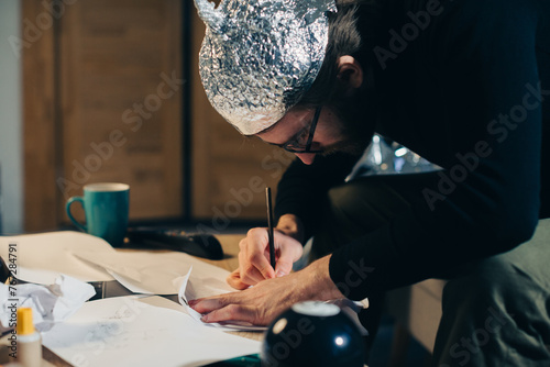 Symbolic Secrets: Man in Tin Foil Headgear Sketching Esoteric Signs