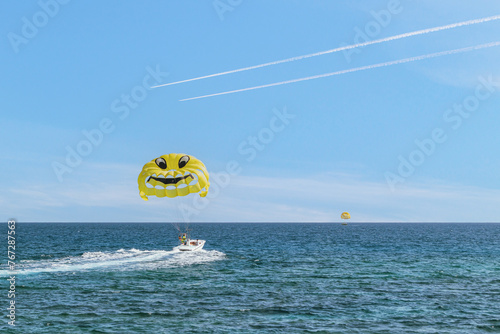 Parasailing in the sea. Flight to parachute. A yellow parasail parachute with a smiley face being pulled by a motorboat © Armands photography