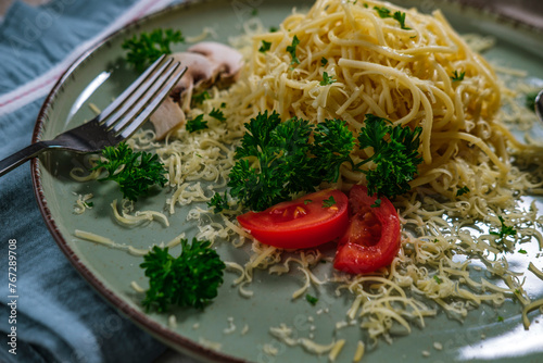 noodles spagetti with butter served with cheese, tomatoes , mushroom and parsley on table cloth, blue napkin, light green ceramic plate photo