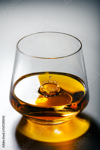 A glass of whiskey with a splash from a falling drop inside. Luxury alcohol concept