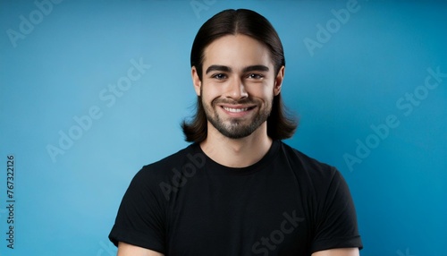 Handsome brunette young man in simple black t-shirt with curly hair smiling to the camera isolated on blue background with copy space, good looking model portrait  © Marko