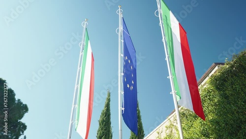 Flags of Italy and European Union against blue sky background, symbol of unity between the countries of Europe, democracy, financial agreements, trade and common currency concept photo