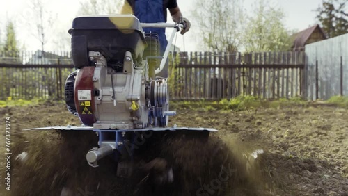 Gardener prepping land for crops with a motorized tiller. Farmer works the land with a tiller in a rural backyard