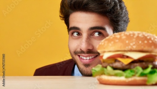 man peeking atcheeseburger on table against yellow background