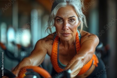 Senior woman with gray hair engaging in a workout on an exercise bike, showing focus and determination photo