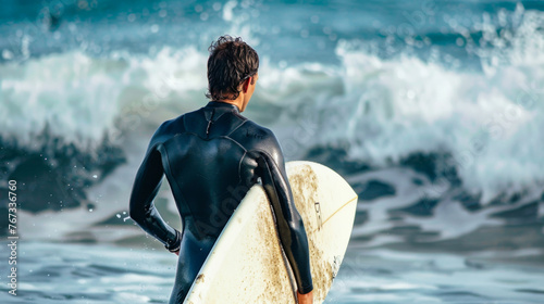 Surfer in wetsuit holding surfboard preparing to enter the ocean waves © Paula
