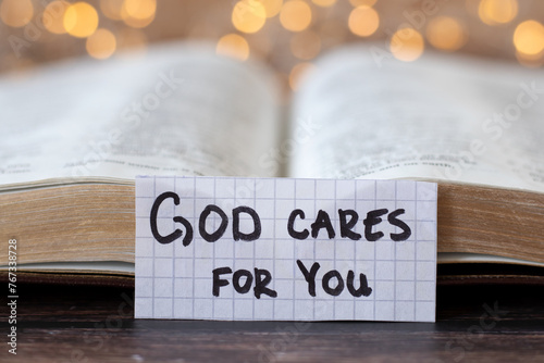 God cares for you, handwritten quote in front of open holy bible book with bokeh light background. Close-up. Christian biblical concept of Jesus Christ's love, promise, grace, and salvation.