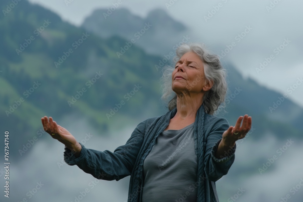 Senior gray haired woman doing breathing exercise in nature on early morning with fog and mountains in background. Senior gray haired woman doing breathing exercise in nature on early morning with fog and mountains in background.
