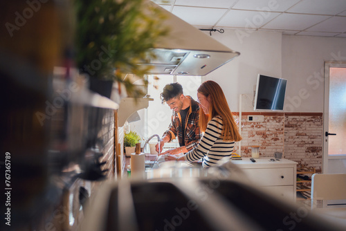 A man and woman washing dishes and glasses in a kitchen