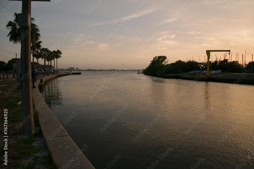 Fototapeta premium Leading lines Wide view south out of City of Gulfport Municipal Marina. Calm Blue Water with small Ripple waves. Curved seawall and boats in the background. With cloudy sky in Gulfport, FL. Sunset 