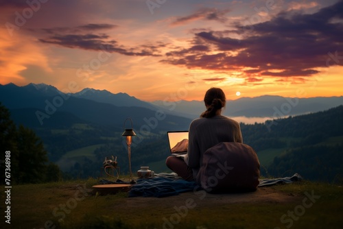 Serene Sunset Work Environment in Nature. Woman using laptop in a tranquil outdoor setting as the sun sets behind the mountains.