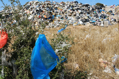 Urban Landfill Site with Scattered Trash and Vegetation.A landfill site filled with assorted garbage and scattered plastic bags, with green shrubs in the foreground. 