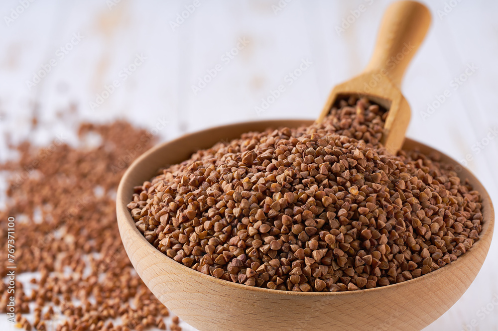 Raw buckwheat are scattered in a wooden bowl close up. Raw buckwheat are scattered in a wooden bowl close up.