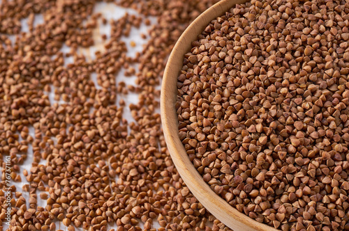 Organic buckwheat are scattered out of the wooden bowl on a light table, selective focus.