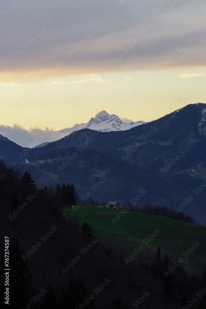 A three peaked mountain in the sunset with cloud cover over them and a small houde in front. A three peaked mountain in the sunset with cloud cover over them and a small houde in front.
