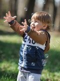 Happy smiling cute toddler delights in chasing floating soap bubbles, bathed in sunlight amidst nature. Love and family concept