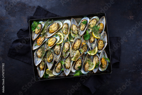 Traditional New Zealand green scallops halved and gratinated with herbs, spices and garlic served in white wine as top view on a rustic baking tray photo