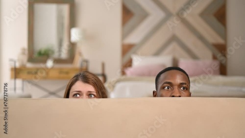 Young couple, woman and man comically hiding behind the sofa, close up