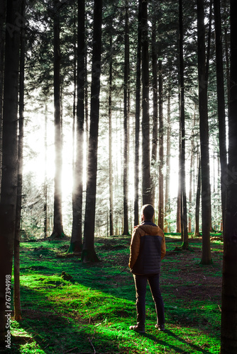 A person in the woods looking at the misterious lighting behind the trees. A man looking at the strange light in the forest.