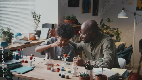 Cheerful African American man talking to little son and ruffling his hair while making DIY solar system model together at home photo