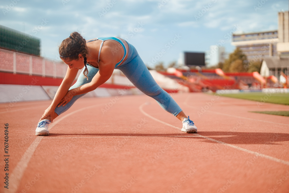 Athletic woman doing stretching exercises on running track at the stadium