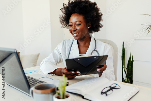 Obraz na plátně Medical doctor working on laptop and desktop computer, networking with people online and sitting at a desk at a hospital