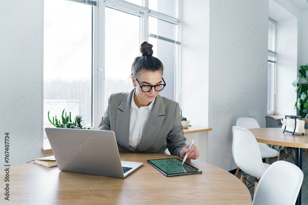 A diligent professional woman focuses on her tablet, utilizing a stylus for precision work, with her laptop ready beside her in a minimalist office. A diligent professional woman focuses on her tablet, utilizing a stylus for precision work, with her laptop ready beside her in a minimalist office.