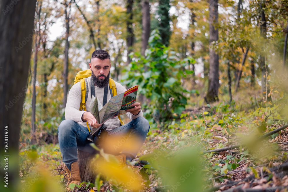 Obraz premium During his woodland hike, a hipster enjoys a rest, sitting on a tree stump while consulting a paper map to plan his route.