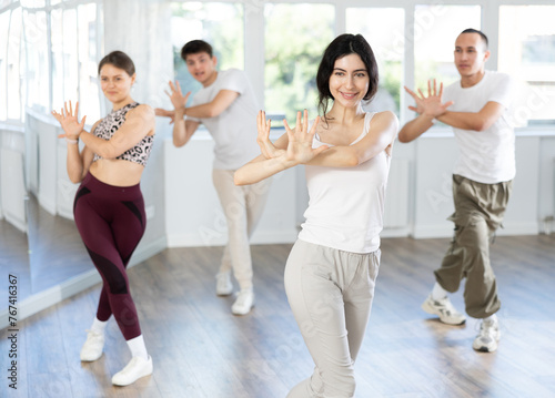 Positive young girl dancing vigorous swing with other people during group training in dance hall