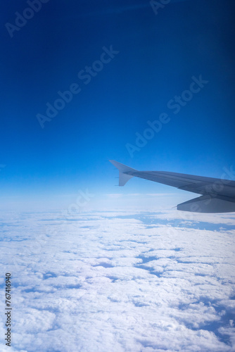 Wing of airplane soaring above fluffy clouds, captured from window seat. Aerial view showcases serene beauty of the sky. 